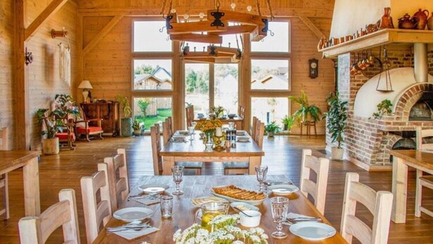 A dining area with a wooden table set for six, surrounded by chairs. There is a brick oven in the background. - Wooden Summer Houses, Bobolin (Darlowo)