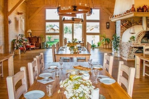 A dining area with a wooden table set for six, surrounded by chairs. There is a brick oven in the background. - Wooden Summer Houses, Bobolin (Darlowo)