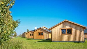 A row of wooden cabins with pitched roofs, arranged in a grassy field. - Wooden Summer Houses, Bobolin (Darlowo)