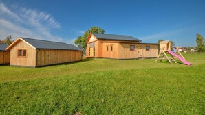 A wooden building with a large open area in front, a slide, and a fenced area. - Wooden Summer Houses, Bobolin (Darlowo)