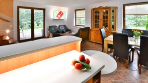 A modern kitchen with a white countertop, a dining area with a wooden table and chairs, and a view of the outdoors through large windows. - Comfortable, Large Holiday Home With a Garden (Malechowo)