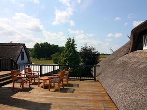 Eine Holzterrasse mit Gartenmöbeln und einem Gebäude mit einem Reetdach.