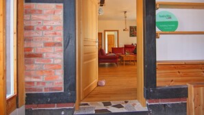Une porte en bois donne sur un salon où se trouvent un canapé rouge et une table basse en bois.