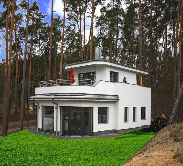 Una casa moderna de dos pisos con techo plano, ventanas grandes y un balcón.