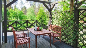 Un terrazzo in legno con un tavolo e due sedie, immerso nel verde e alberi.