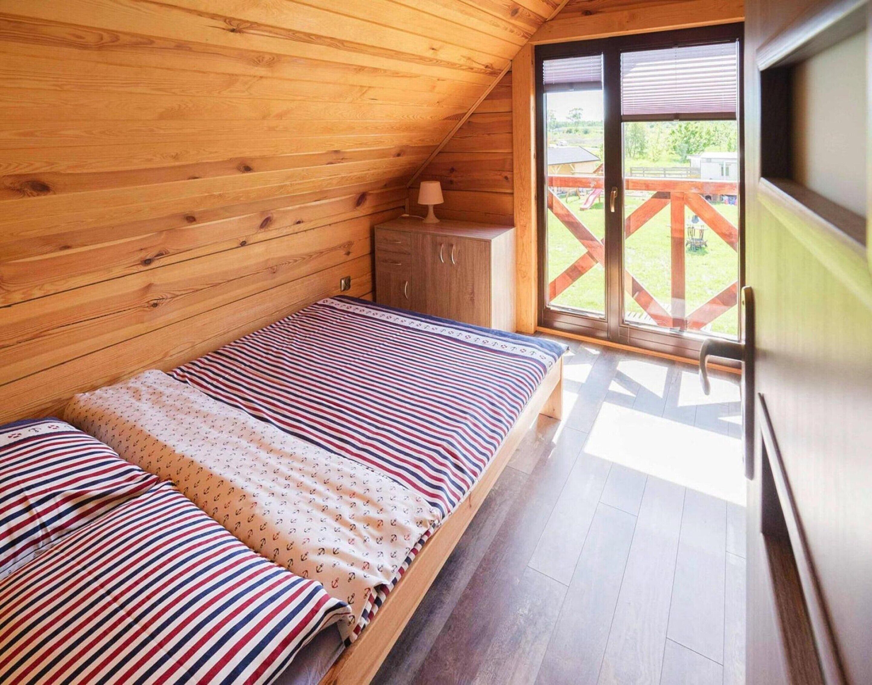 Een houten kamer met een bed, een klein kastje en een schuifglazen deur naar een buitenruimte.