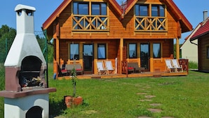 Una cabaña de madera con chimenea, dos balcones y un patio con mobiliario exterior.