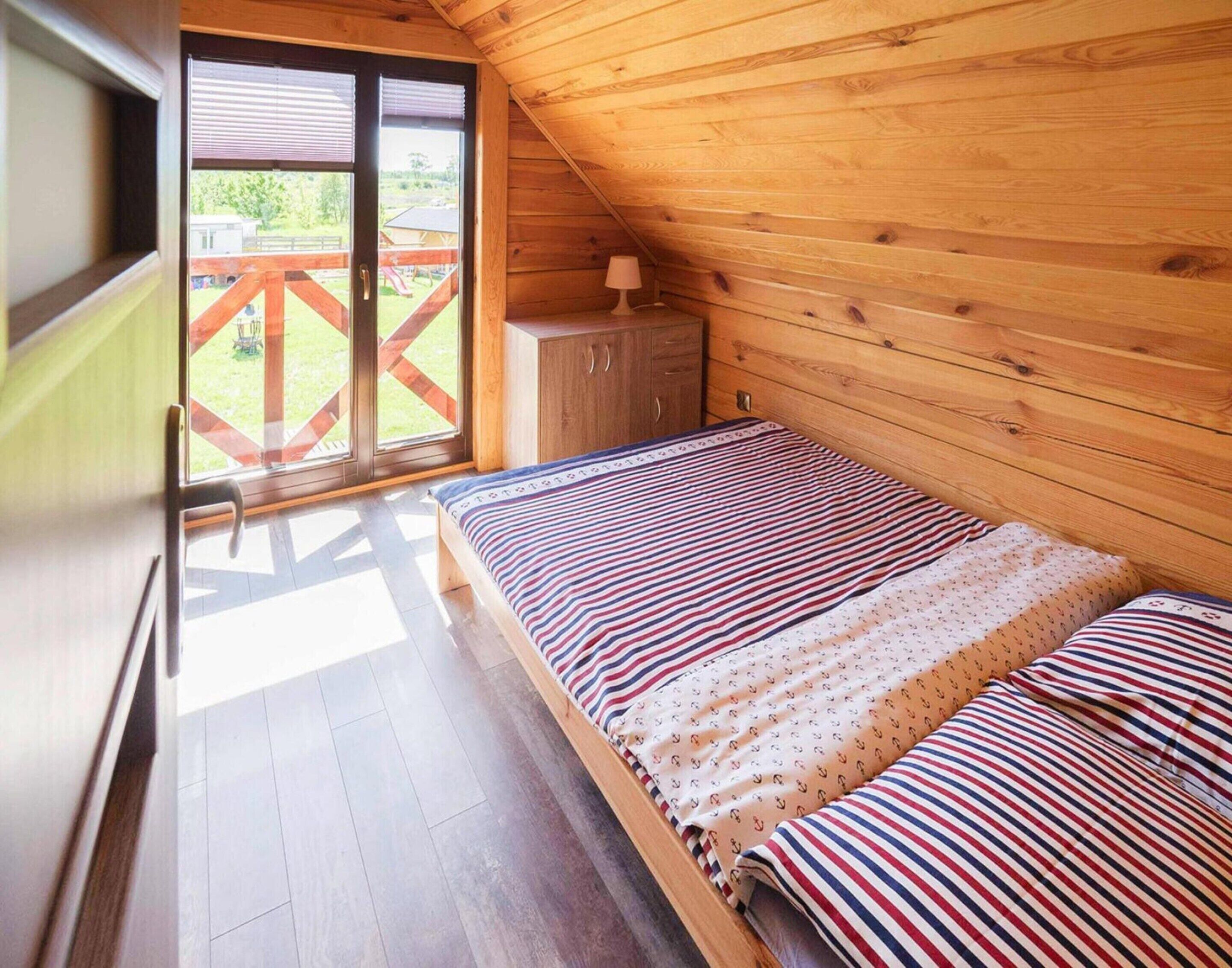 Een slaapkamer in een houten hutje, met een bed, een klein kastje en een schuifdeur naar een balkon.