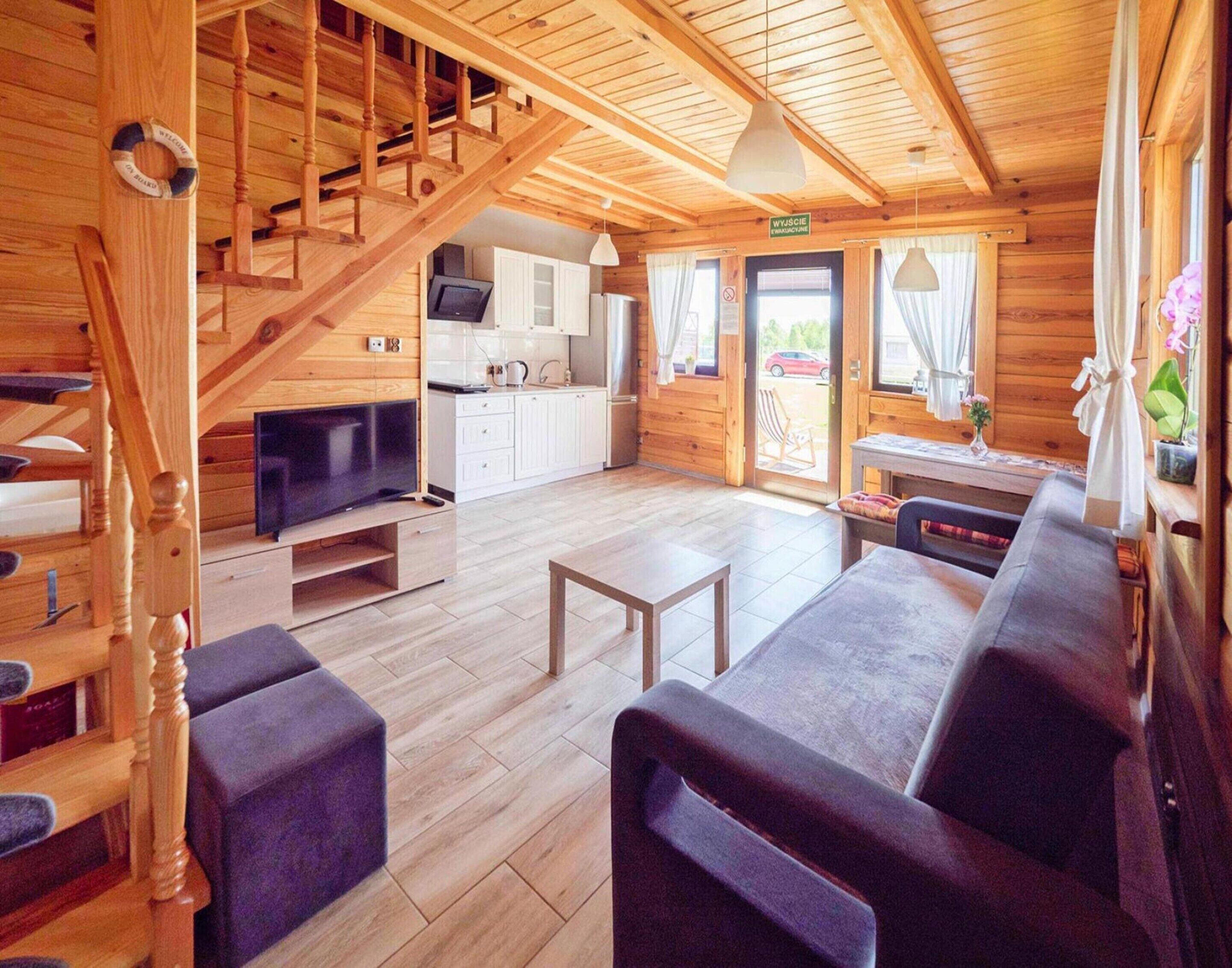 Ein Holzinnenraum mit Treppe, einer Couch, einem Fernseher und einer Küchenzeile.