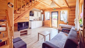 Un interior de madera con una escalera, un sofá, un televisor y una zona de cocina.