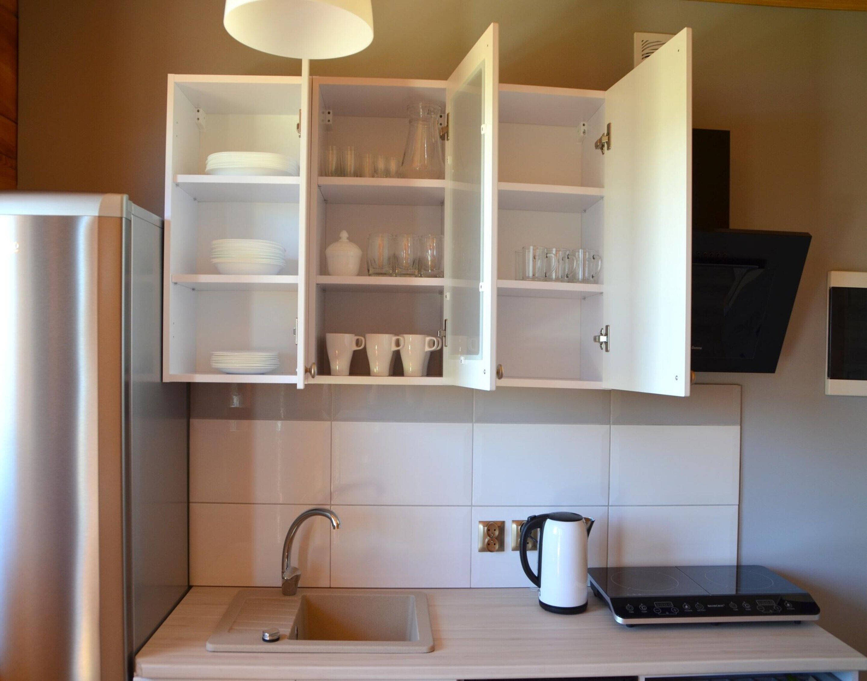 A kitchen with a built-in oven, a sink, and a cabinet with dishes and glasses.