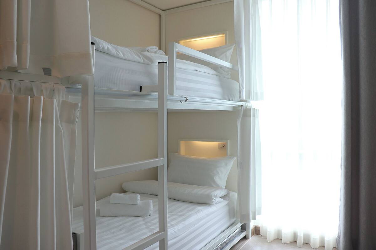 Ein Schlafraum mit Etagenbett, weißer Bettwäsche und einer Nachttischlampe.