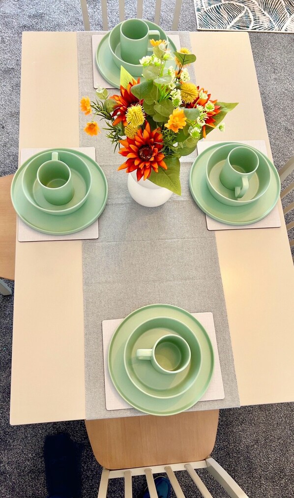 A table set with green plates, cups, and a vase of flowers.