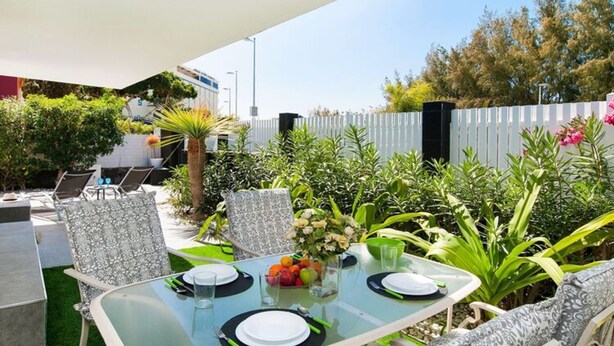 An outdoor dining area with a glass table, chairs, and a white fence in the background. - Vacation Home, San Agustin (San Bartolomé de Tirajana)