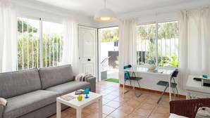 A bright living room with a grey sofa, a small white table, and a dining area with a white table and chairs. - Vacation Home, San Agustin (San Bartolomé de Tirajana)