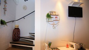 Una escalera con una pared blanca, un televisor montado encima y un estante con objetos decorativos.