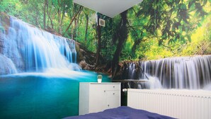 Un dormitorio con un mural de cascada y bosque, un aparador blanco y un radiador.