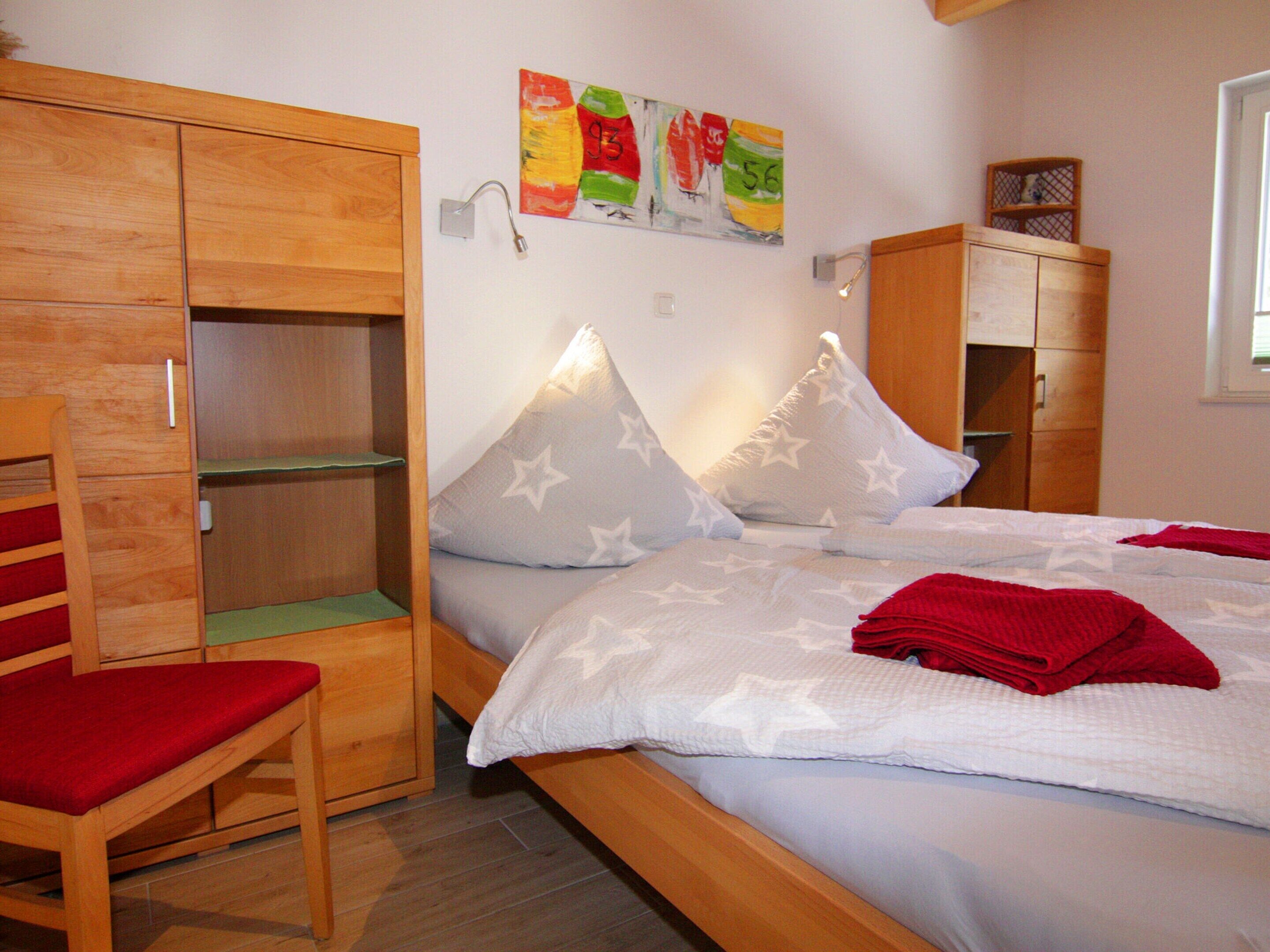 Ein Schlafzimmer mit einem Bett, einem Holzschrank, einem Stuhl und einer Wand mit farbenfroher Kunst.