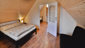 A bedroom with a wooden sloped ceiling, a bed with a floral bedspread, a bedside lamp, and a white door leading to another room. - Comfortable Holiday Cottages in Ustronie Morskie (Ustronie Morskie)
