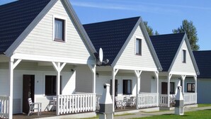 A row of white cabins with dark roofs, each featuring a porch with white railings and outdoor seating. - Comfortable Holiday Cottages in Ustronie Morskie (Ustronie Morskie)