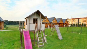A playground with a slide and climbing structures, surrounded by residential buildings with sloped roofs. - Comfortable Holiday Cottages in Ustronie Morskie (Ustronie Morskie)