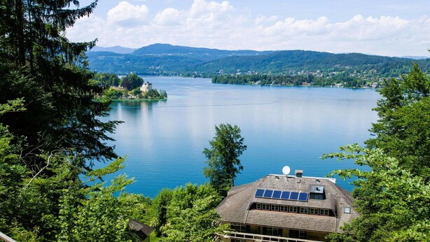 Une propriété située au bord d’un lac, avec une maison dotée d’un toit en pente, de panneaux solaires et d’un balcon agrémenté de parasols.