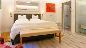 Une chambre d’hôtel moderne avec un grand lit, un banc, une douche en verre et un mur d’accent rouge.
