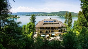 Un bâtiment situé au bord d’un lac, doté d’un balcon incurvé, entouré d’une forêt dense et offrant une vue sur un lac paisible et des montagnes lointaines.
