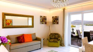 Un salon comprenant un canapé, un fauteuil, un tapis à motifs verts et blancs, un lustre et des œuvres d’art accrochées aux murs.