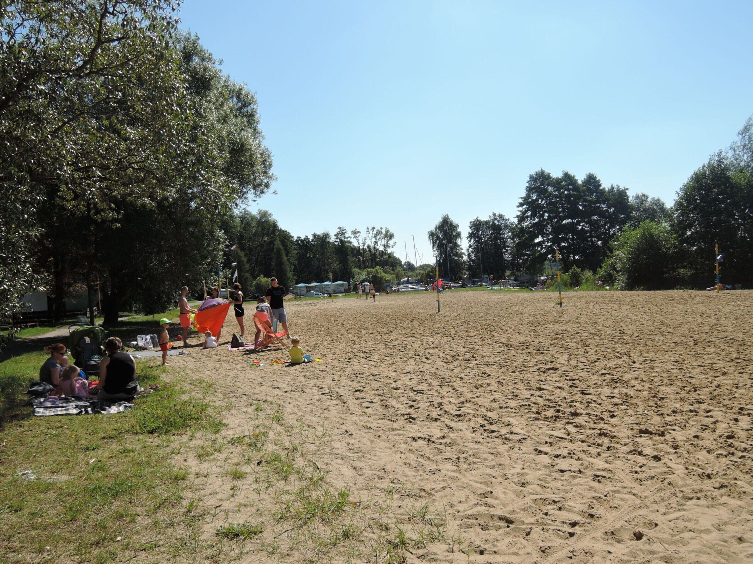 A sandy beach with people sitting and playing.