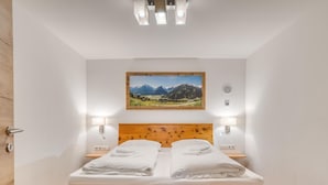 A neatly made bed with white linens and towels, a wooden headboard, and a framed landscape painting above it. - Chalet in Neukirchen With Mountain Views (Neukirchen am Grossvenediger)