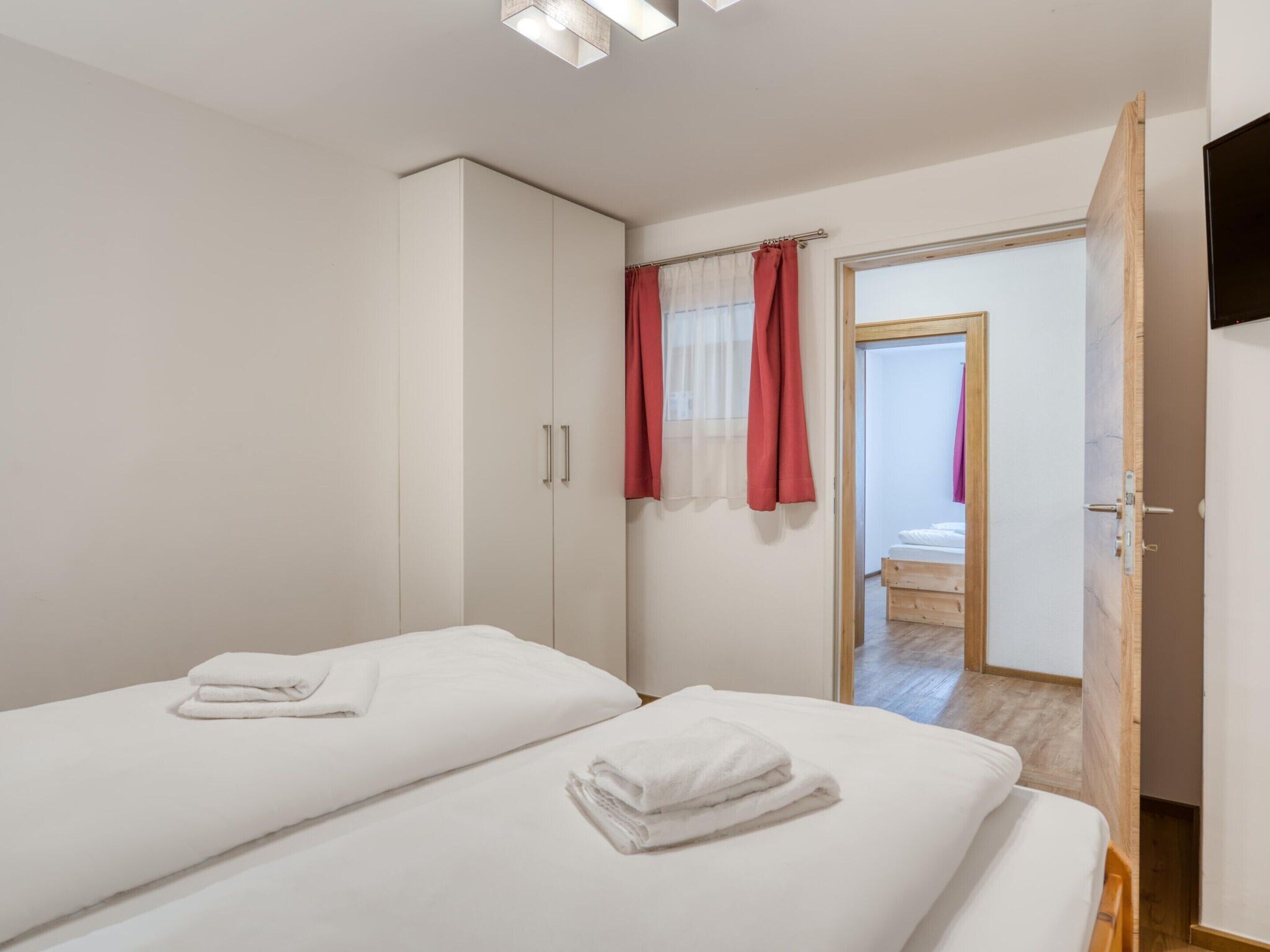 A bedroom with two beds, a wardrobe, and a bathroom visible through an open door.
