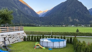 A swimming pool with a slide, surrounded by a stone wall, set against a mountainous backdrop. - Chalet in Neukirchen With Mountain Views (Neukirchen am Grossvenediger)