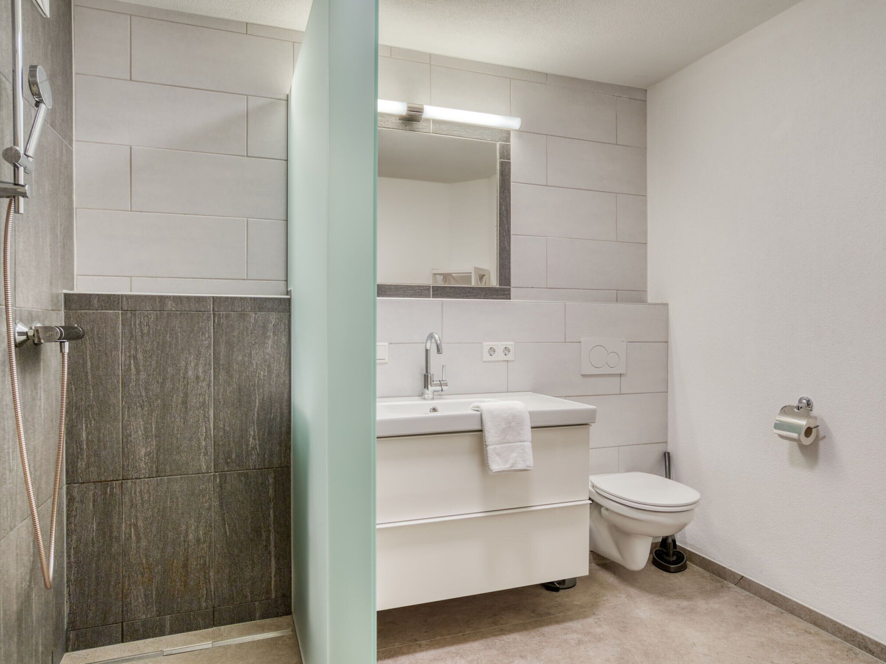 A modern bathroom with a shower, toilet, and sink.