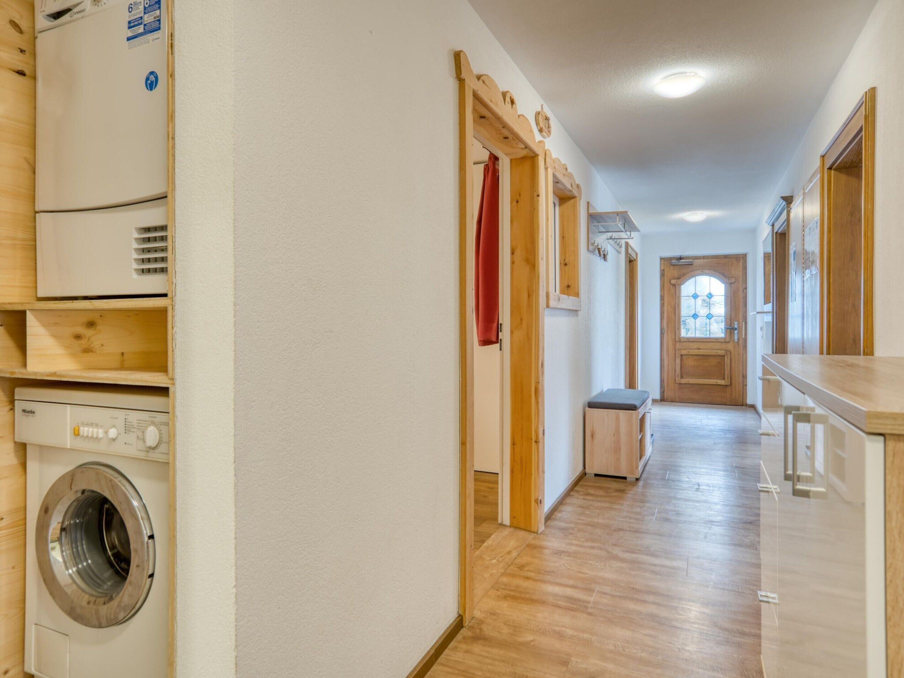 A laundry room with a washing machine and dryer, wooden flooring, and a door leading to another room.