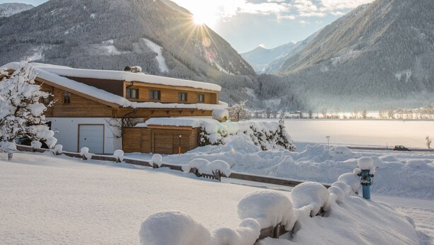 A wooden chalet with a sloped roof, surrounded by snow-covered mountains and a lake. - Chalet in Neukirchen With Mountain Views (Neukirchen am Grossvenediger)