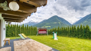 A wooden deck with a table and benches, a swing set, and a slide, overlooking a mountainous landscape. - Chalet in Neukirchen With Mountain Views (Neukirchen am Grossvenediger)