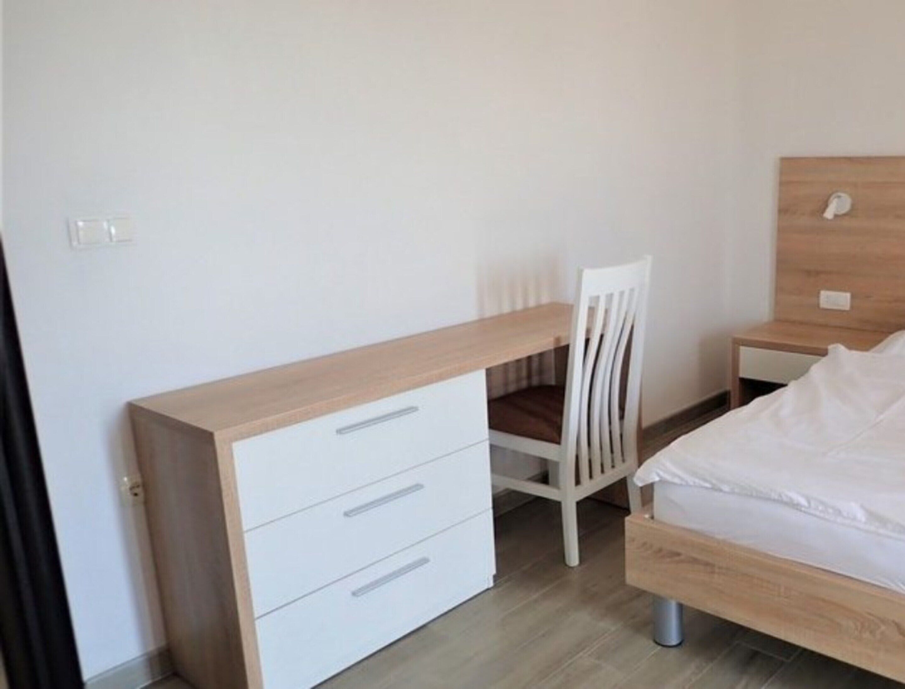 Une chambre à coucher avec un lit en bois, un bureau blanc avec des tiroirs, une chaise blanche et une table de chevet.
