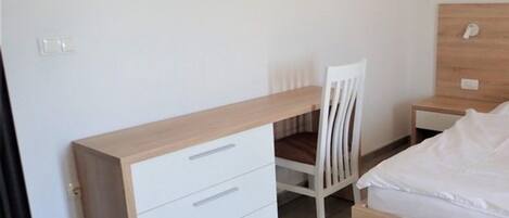 Une chambre à coucher avec un lit en bois, un bureau blanc avec des tiroirs, une chaise blanche et une table de chevet.