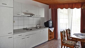 Une cuisine avec des meubles blancs, une cuisinière et un évier. On y trouve une table à manger en bois, accompagnée de chaises.