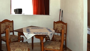 Un coin repas avec une table en bois et quatre chaises, une fenêtre avec des rideaux et un téléviseur posé sur le rebord de la fenêtre.