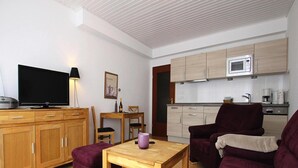 A modern living room with a wooden floor, a purple sofa, a wooden coffee table, and a TV on a wooden cabinet. - Appartement in Westerland auf Sylt (Sylt)