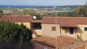 Un quartiere residenziale con tetti in tegole di terracotta, un'antenna parabolica e vista sul mare e edifici in lontananza.