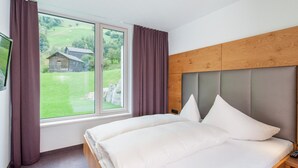 Un dormitorio con cama, cabecera de madera, ventana con cortinas y vistas a una casa y follaje exterior.