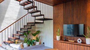 A modern living room with a staircase, a flat-screen TV, and potted plants. - Nala Villa by Betterplace (Canggu)