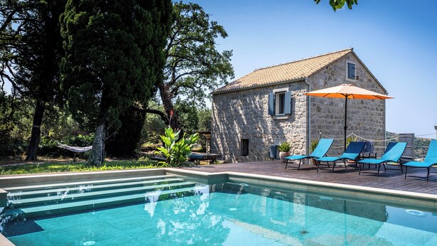 A stone building with a tiled roof, a swimming pool with clear blue water, and several blue lounge chairs. - Rustic 4-bedroom villa with all the modern amenities in quiet surrounding  (Croatia)
