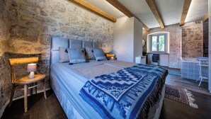A bedroom with a stone wall, wooden beams, a bed with patterned bedding, a bedside lamp, and a small table with a chair. - Rustic 4-bedroom villa with all the modern amenities in quiet surrounding  (Croatia)