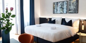 A hotel room with a large bed, a bedside table, a chair, and a window with curtains. - Urbanauts Studios in Wien (Vienna)