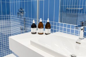 A bathroom with a white sink, three bottles of Saint Charles products, and a blue tiled wall. - Urbanauts Studios in Wien (Vienna)