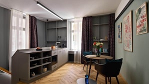 A compact kitchen with modern appliances, a dining area with a round table and chairs, and a bookshelf with decorative items.